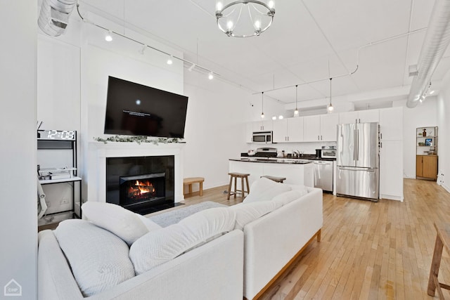 living area featuring rail lighting, a fireplace with flush hearth, light wood-style flooring, and an inviting chandelier