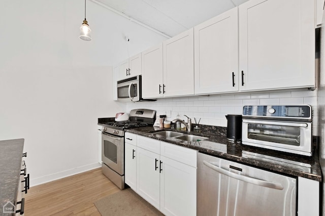 kitchen with backsplash, appliances with stainless steel finishes, light wood-style floors, white cabinetry, and a sink