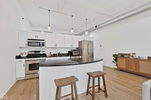 kitchen featuring a breakfast bar, white cabinetry, appliances with stainless steel finishes, light wood finished floors, and tasteful backsplash