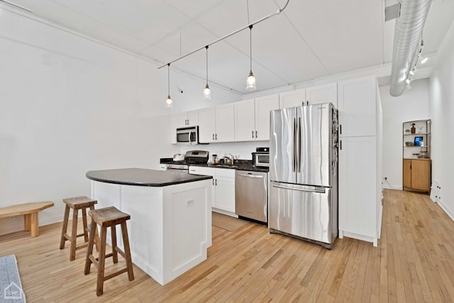 kitchen featuring stainless steel appliances, dark countertops, white cabinetry, and light wood finished floors