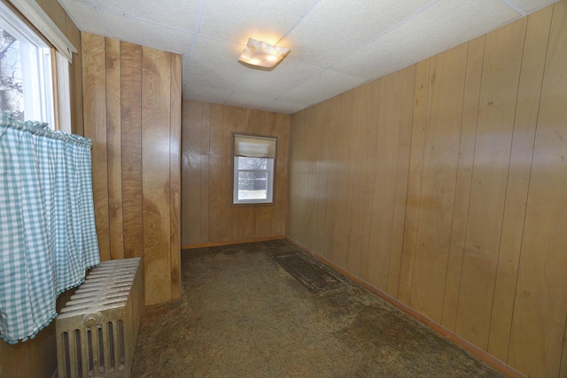 unfurnished room featuring carpet floors, wood walls, and radiator heating unit