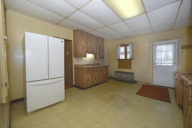 kitchen with a drop ceiling, a sink, freestanding refrigerator, brown cabinets, and radiator heating unit