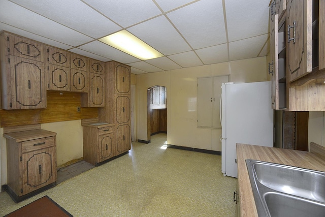 kitchen featuring arched walkways, a drop ceiling, freestanding refrigerator, light floors, and a sink