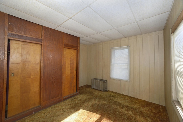 unfurnished bedroom with a drop ceiling, multiple windows, carpet, and radiator