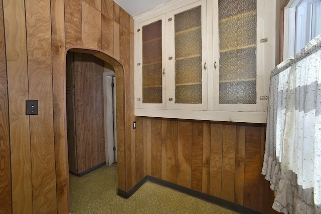 corridor featuring wood walls, arched walkways, and tile patterned floors