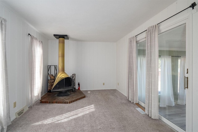 unfurnished living room featuring visible vents, carpet floors, a healthy amount of sunlight, and a wood stove