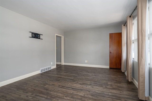 empty room with dark wood-style floors, visible vents, and baseboards