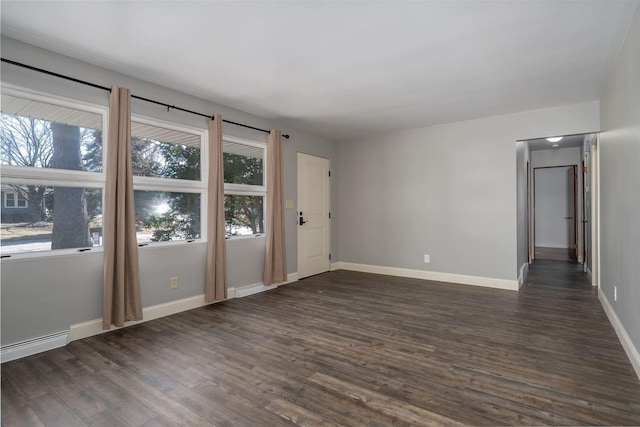 spare room featuring a baseboard heating unit, dark wood-type flooring, and baseboards