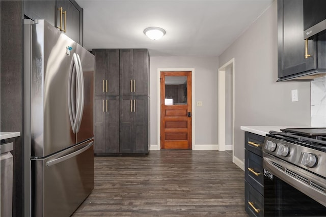 kitchen featuring baseboards, dark wood finished floors, light countertops, stainless steel appliances, and wall chimney exhaust hood