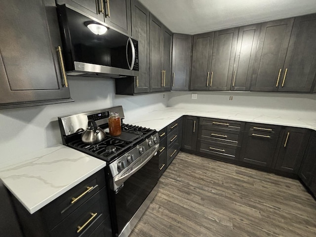 kitchen with dark cabinetry, dark wood-type flooring, gas stove, and light stone countertops