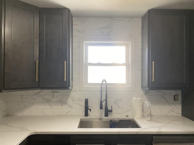 kitchen with light stone counters, backsplash, and a sink