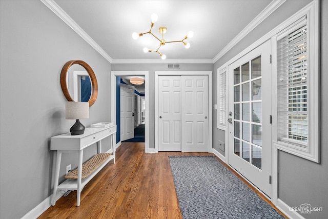 foyer entrance with baseboards, visible vents, wood finished floors, crown molding, and a chandelier