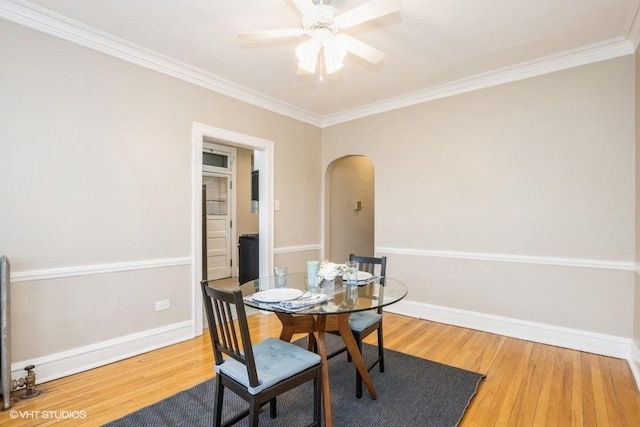 dining room with arched walkways, ornamental molding, wood finished floors, and baseboards