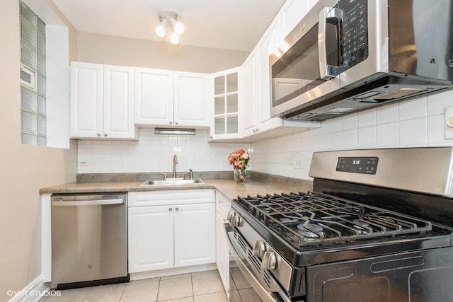 kitchen featuring stainless steel appliances, tasteful backsplash, light tile patterned flooring, white cabinets, and a sink