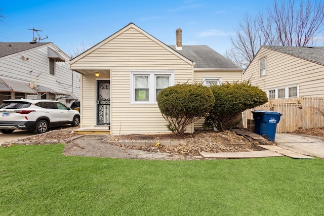 view of front of house featuring roof with shingles, fence, a chimney, and a front lawn