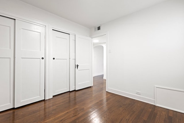 unfurnished bedroom featuring baseboards, visible vents, arched walkways, dark wood-type flooring, and two closets