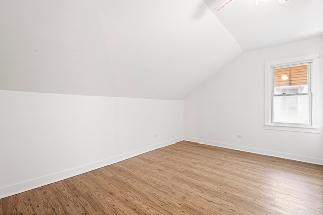 additional living space featuring vaulted ceiling, light wood-style flooring, and baseboards