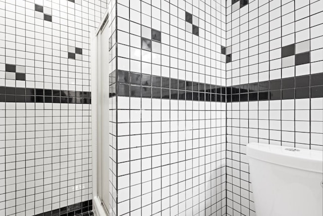 full bath featuring tiled shower, toilet, and tile walls