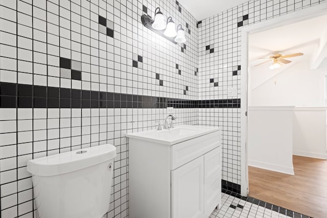 bathroom featuring ceiling fan, toilet, wood finished floors, vanity, and tile walls