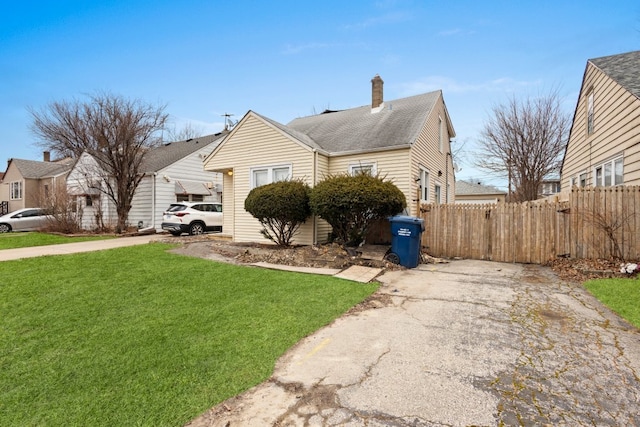 view of front of house with roof with shingles, a front lawn, a chimney, and fence