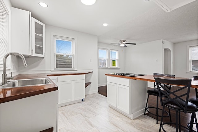 kitchen featuring arched walkways, butcher block counters, a sink, white cabinetry, and a kitchen bar