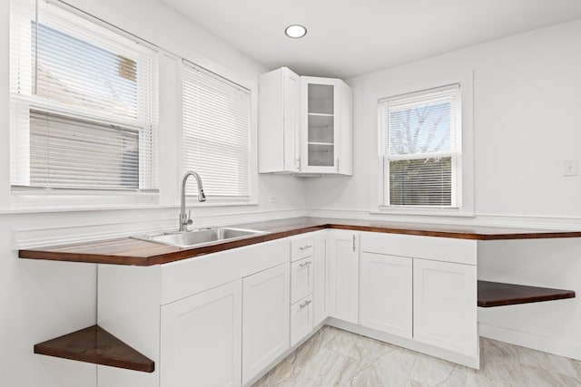 kitchen featuring white cabinets, butcher block counters, glass insert cabinets, marble finish floor, and a sink