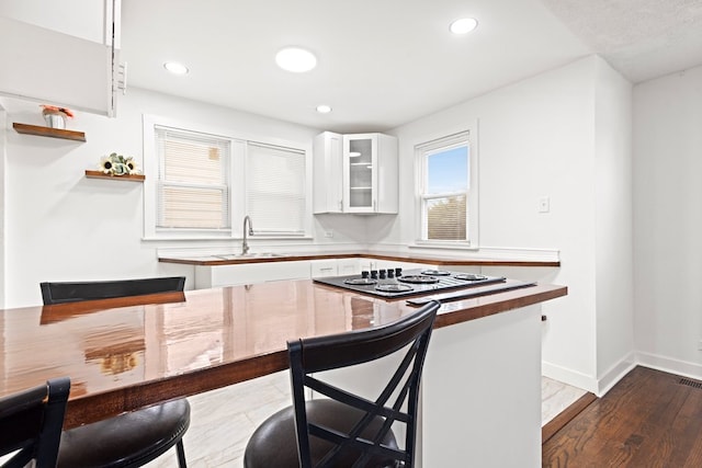 kitchen featuring baseboards, glass insert cabinets, stovetop, white cabinetry, and a sink