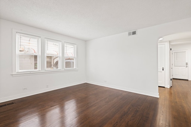 spare room featuring dark wood-type flooring, arched walkways, visible vents, and baseboards