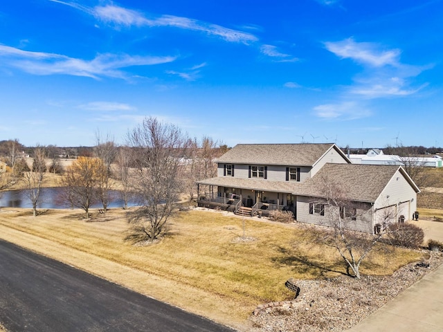 view of front of home with a porch, a front yard, a garage, and a water view