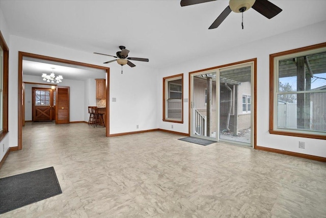 unfurnished living room featuring ceiling fan with notable chandelier, light floors, and baseboards