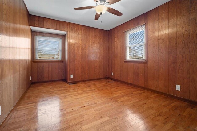 empty room with ceiling fan, light wood-style flooring, and wooden walls