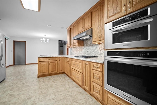 kitchen with decorative backsplash, a peninsula, stainless steel appliances, under cabinet range hood, and a notable chandelier