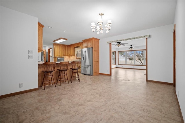 kitchen with refrigerator, a peninsula, baseboards, stainless steel refrigerator with ice dispenser, and a kitchen bar