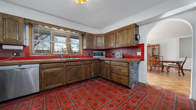 kitchen with tasteful backsplash, arched walkways, dark countertops, stainless steel appliances, and a sink