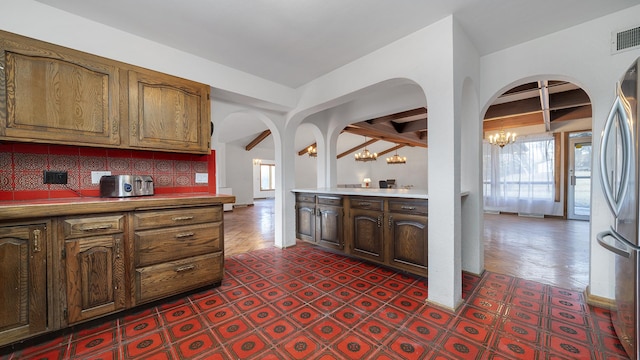 kitchen with arched walkways, tasteful backsplash, freestanding refrigerator, and an inviting chandelier