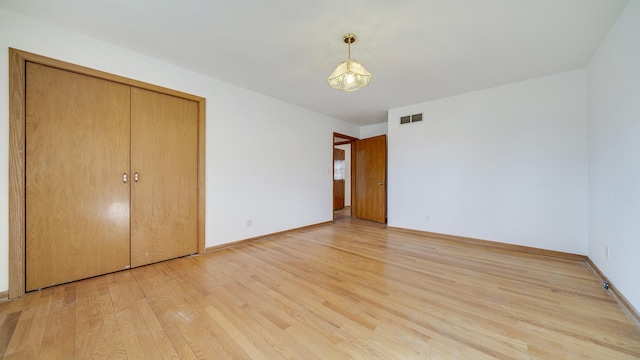 unfurnished bedroom featuring light wood-type flooring, a closet, visible vents, and baseboards