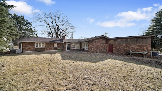 rear view of house with brick siding, a chimney, central AC unit, and a lawn