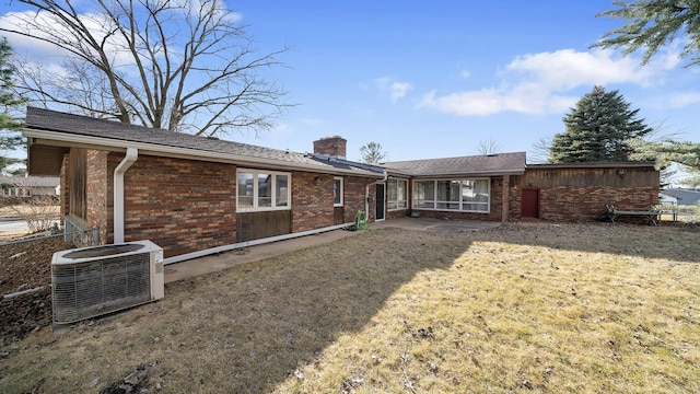 rear view of house featuring a yard, a chimney, cooling unit, and brick siding