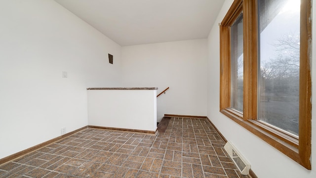 empty room with brick floor, baseboards, and visible vents