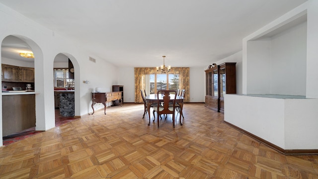 dining room with baseboards, arched walkways, visible vents, and a notable chandelier