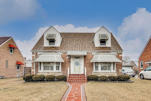 view of front of house featuring brick siding, roof with shingles, and a front yard