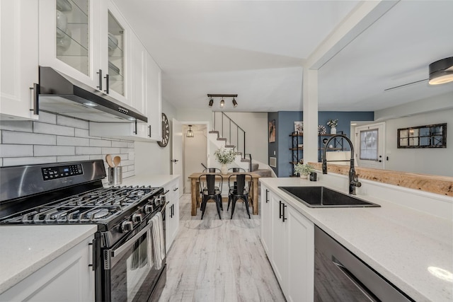 kitchen featuring white cabinets, black range with gas cooktop, a sink, dishwasher, and wall chimney exhaust hood