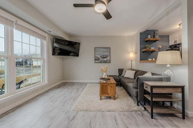 living room with light wood-style flooring, visible vents, baseboards, and a ceiling fan