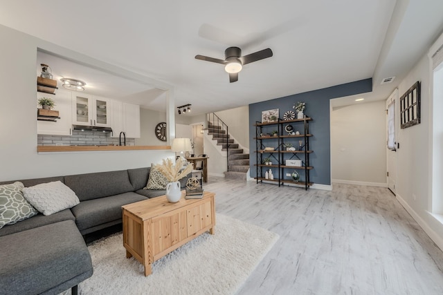 living area featuring a ceiling fan, light wood-type flooring, stairway, and baseboards