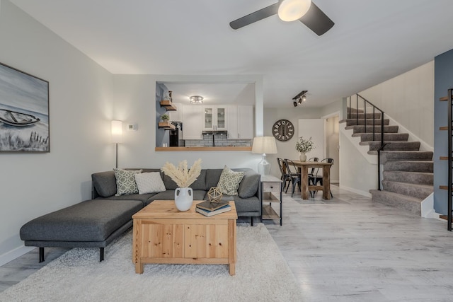 living room featuring ceiling fan, stairway, baseboards, and wood finished floors