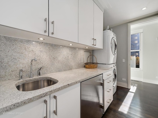 kitchen featuring dark wood-type flooring, stacked washer / dryer, a sink, white cabinets, and tasteful backsplash