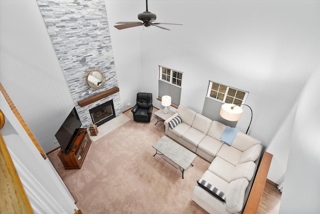 living area featuring ceiling fan, a large fireplace, carpet flooring, a towering ceiling, and baseboards