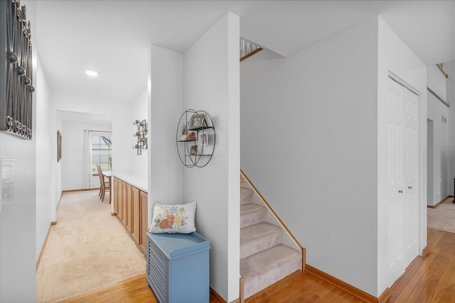 hall with light wood-type flooring, baseboards, and stairs