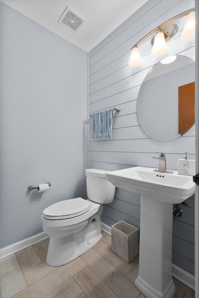 half bathroom featuring baseboards, visible vents, toilet, wood finished floors, and wood walls