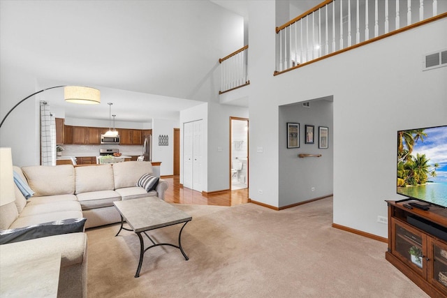 living area with light carpet, a towering ceiling, visible vents, and baseboards